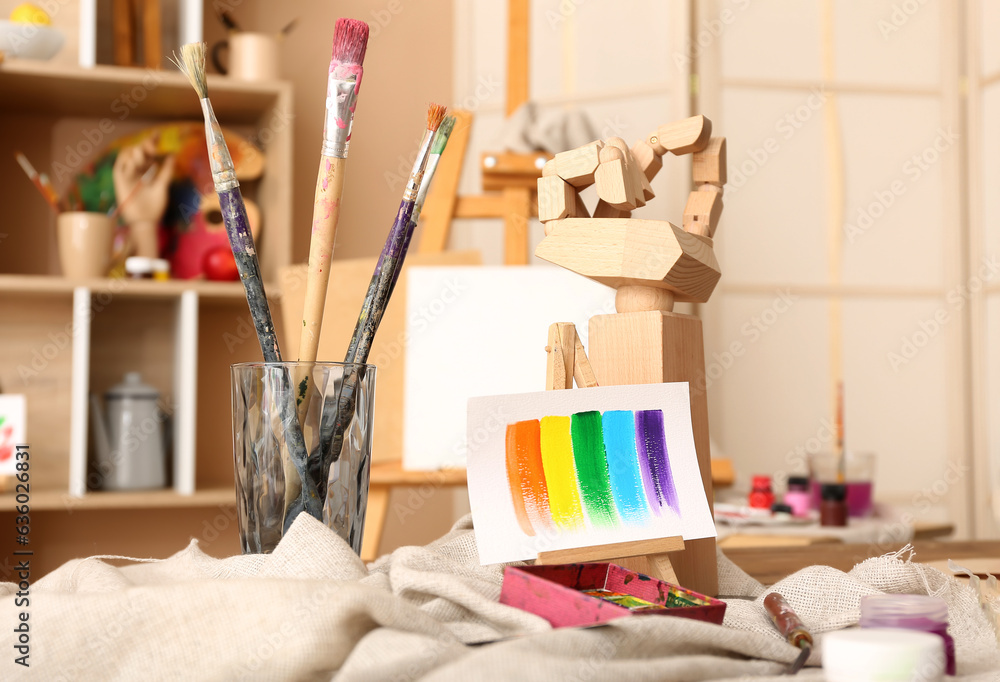 Glass with brushes, paints and mini easel in artists studio