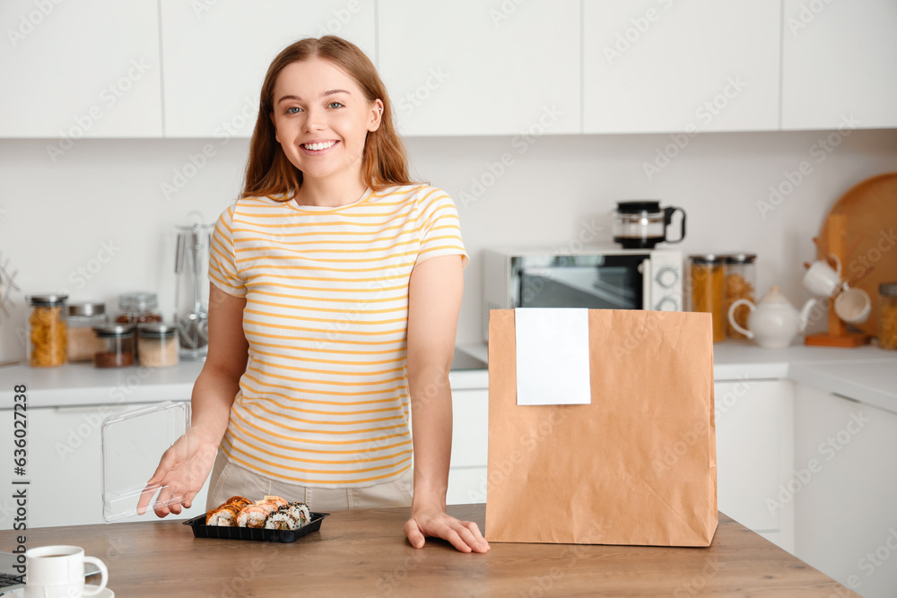 Happy young woman with sushi and paper bag in kitchen