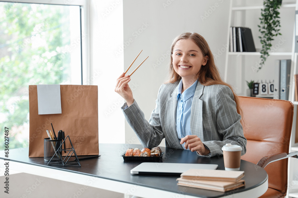 Happy young woman eating sushi in office