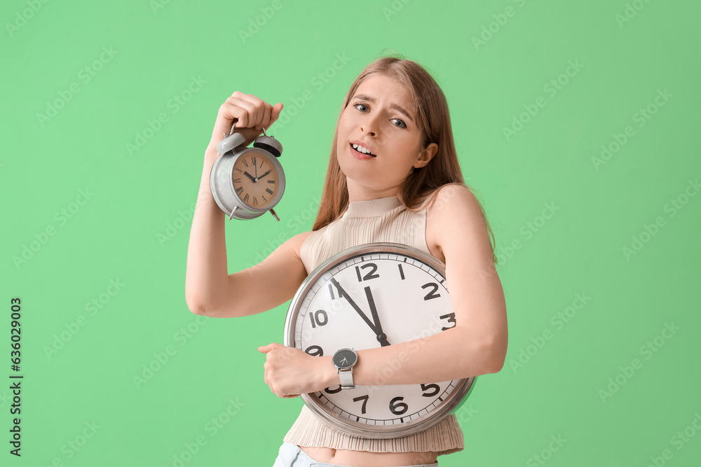 Stressed young woman with clocks on green background. Deadline concept