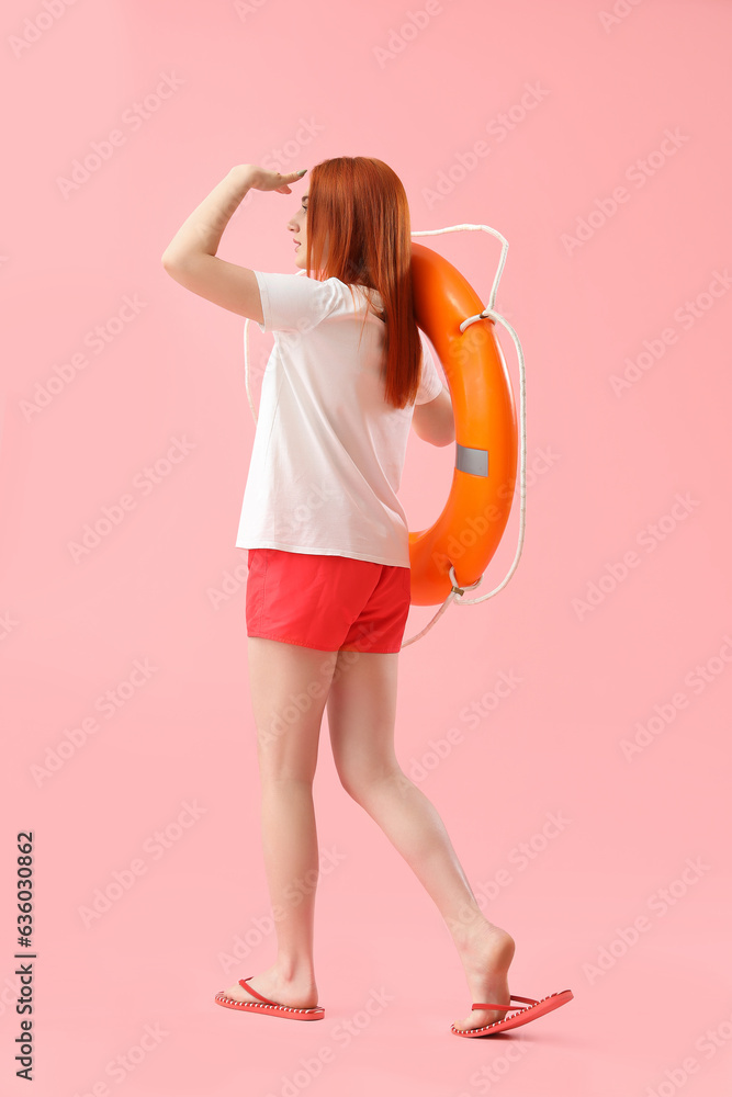 Female lifeguard with ring buoy on pink background, back view