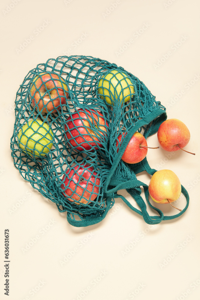 Mesh bag with fresh apples on beige background