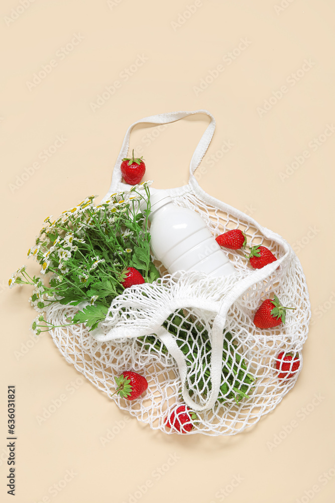 Mesh bag with fresh strawberry and beautiful chamomile flowers on beige background