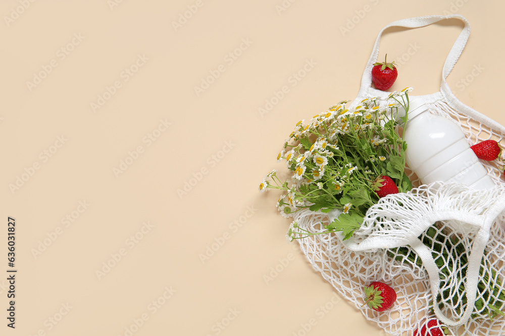 Mesh bag with fresh strawberry and beautiful chamomile flowers on beige background