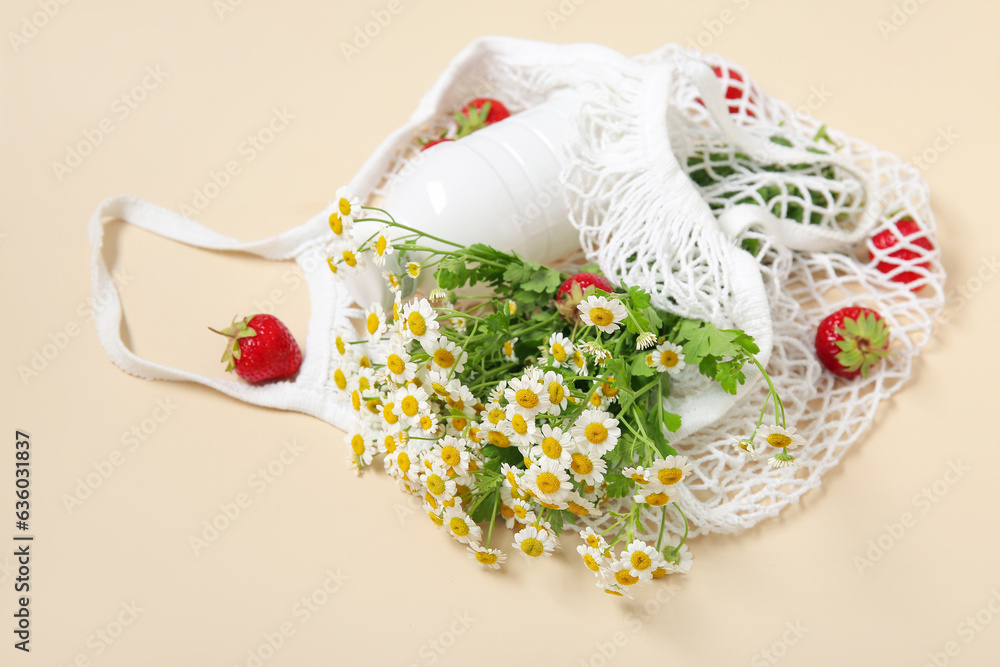 Mesh bag with fresh strawberry and beautiful chamomile flowers on beige background, closeup