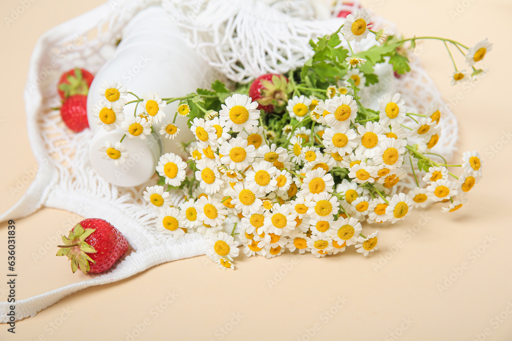 Mesh bag with fresh strawberry and beautiful chamomile flowers on beige background, closeup