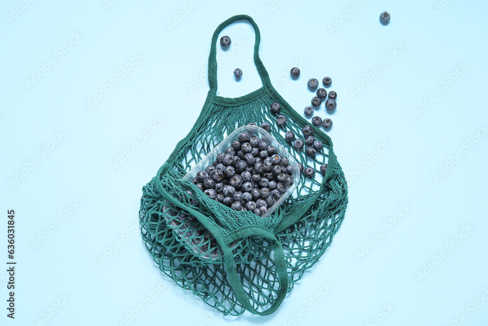 Mesh bag with fresh blueberry in plastic container on blue background