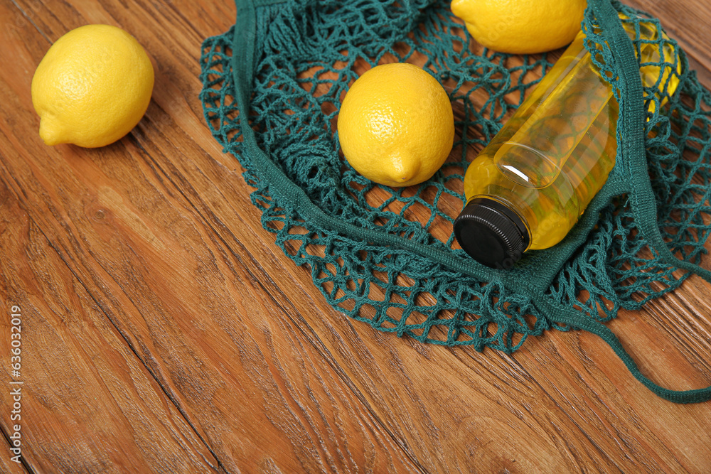 Mesh bag with fresh lemons and bottle of juice on wooden background, closeup