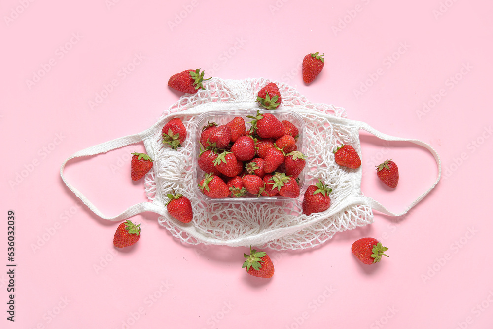 Mesh bag with fresh strawberry in plastic container on pink background