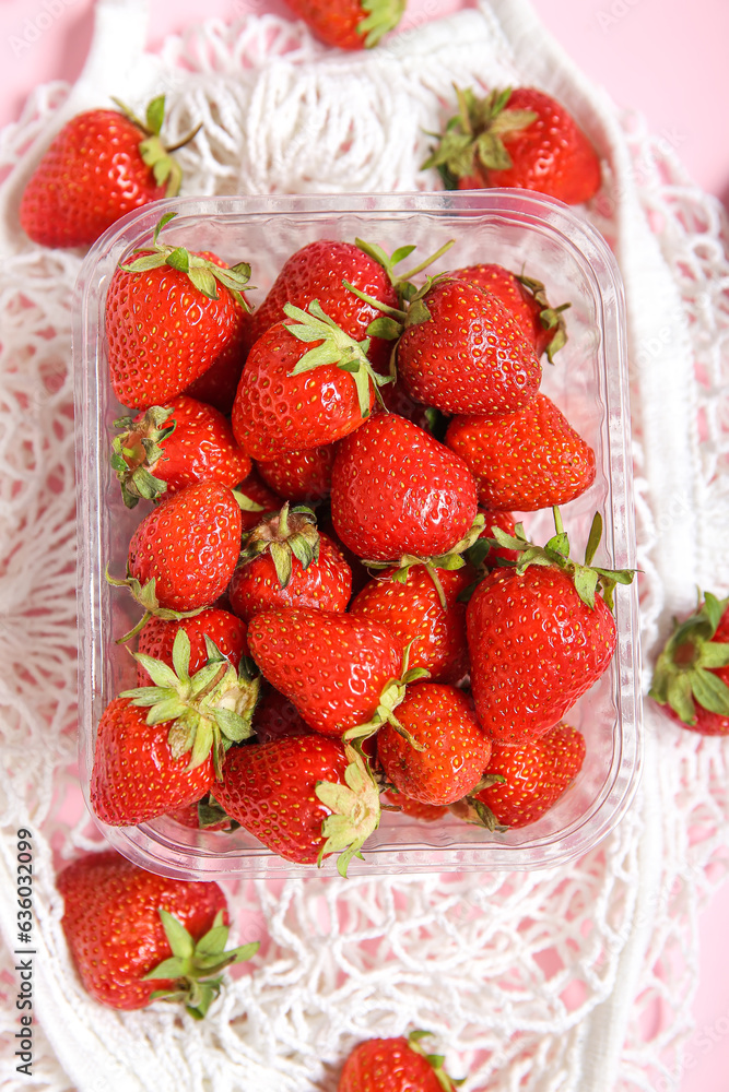 Mesh bag with fresh strawberry in plastic container on pink background, closeup