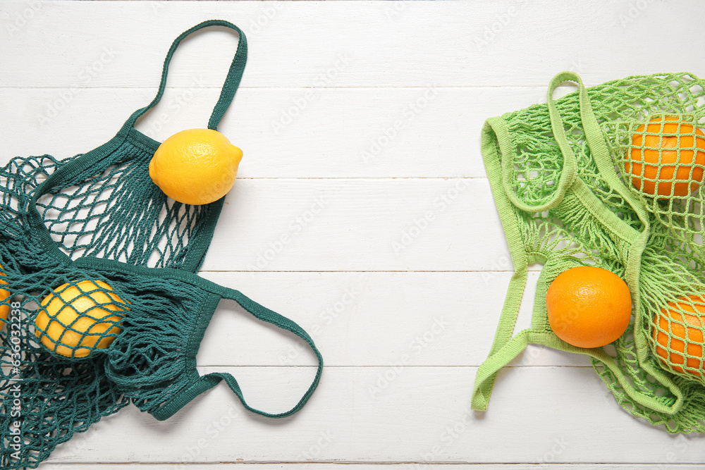 Mesh bags with fresh lemons and oranges on light wooden background