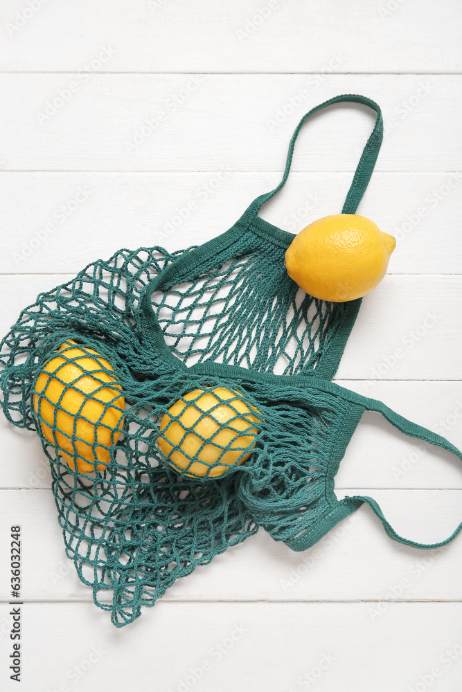 Mesh bag with fresh lemons on light wooden background