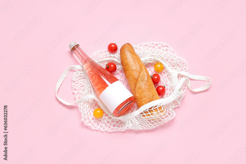 Mesh bag with fresh tomatoes, baguette and bottle of juice on pink background