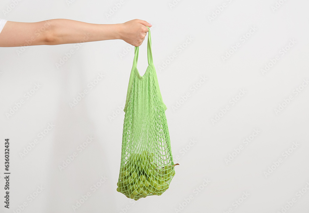 Female hand holding mesh bag with fresh grapes on light background