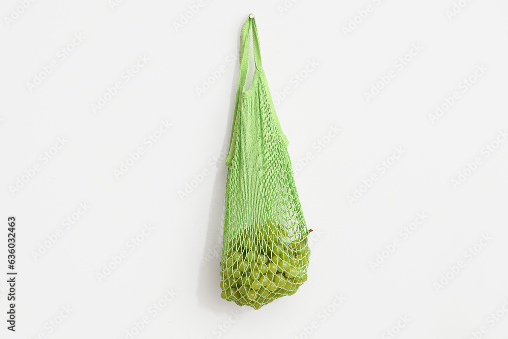 Mesh bag with fresh grapes hanging on light wall in room