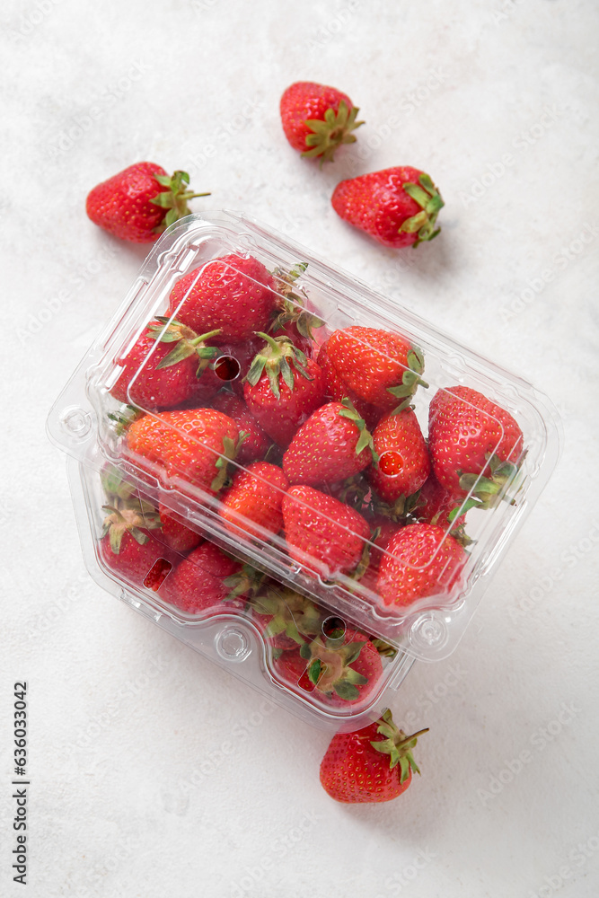 Plastic containers with fresh strawberry on light background