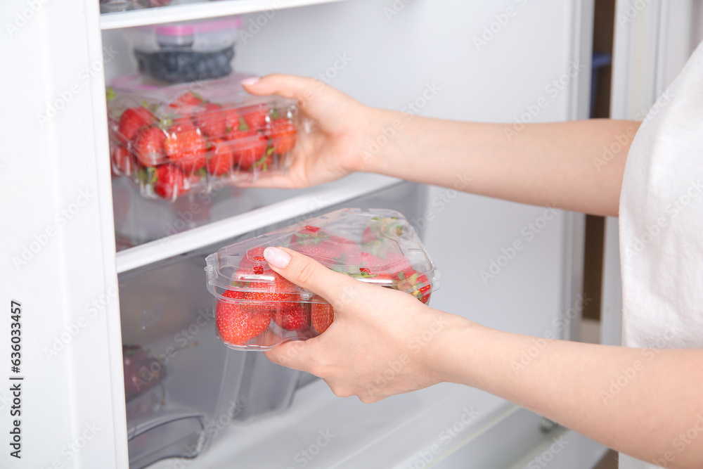 Woman taking strawberry in plastic container from refrigerator, closeup