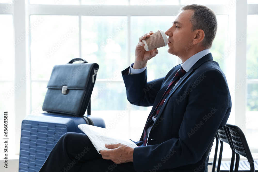 Mature businessman with newspaper drinking coffee in hall of airport