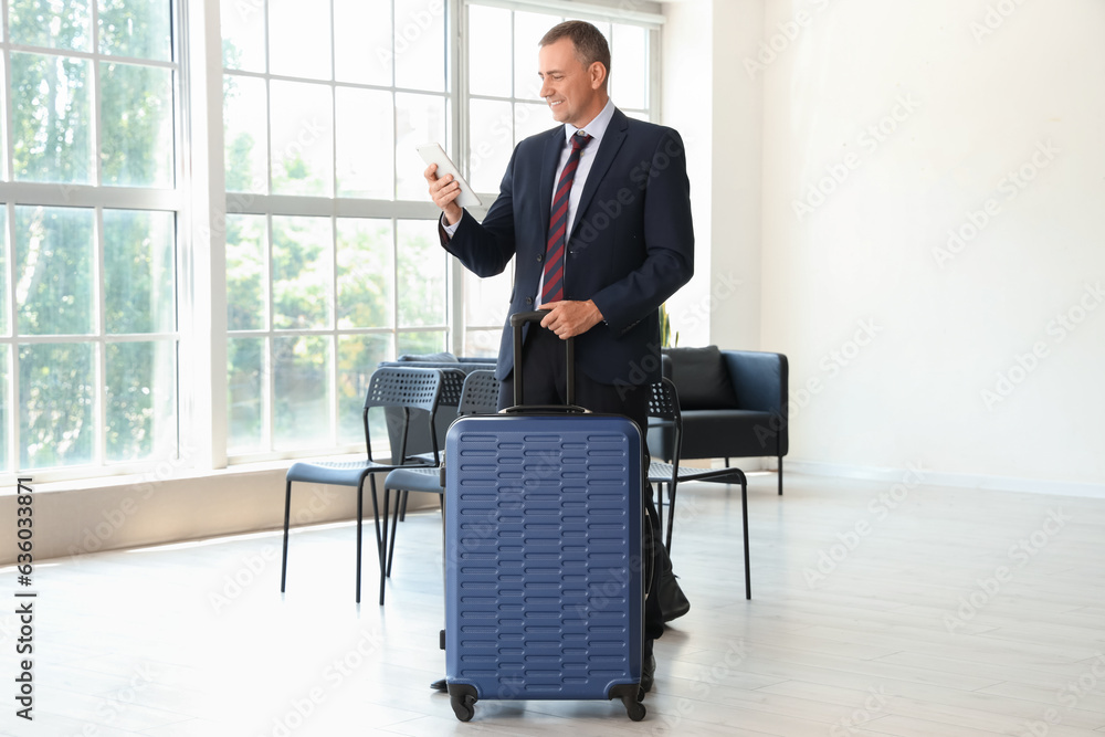 Mature businessman with tablet computer and suitcase in hall of airport