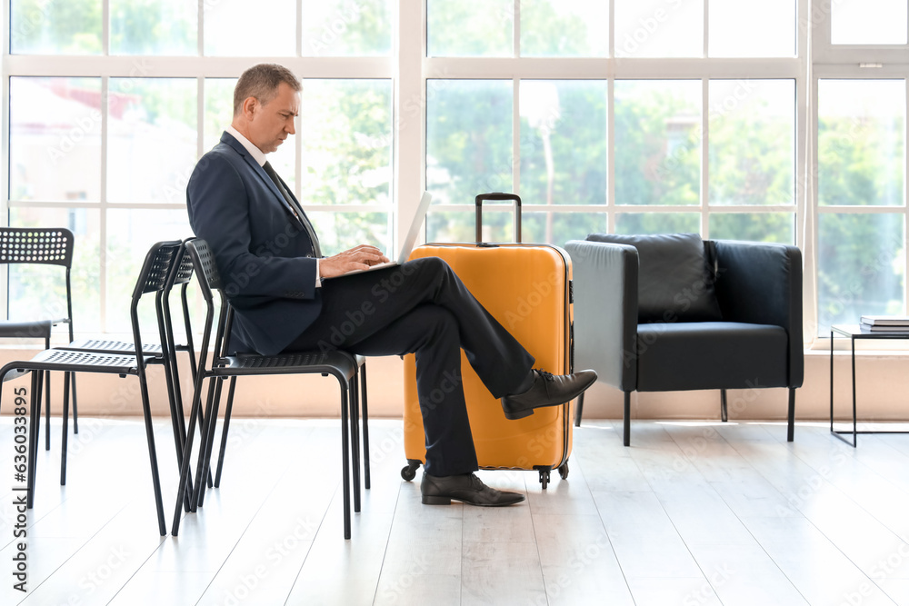 Mature businessman using laptop in hall of airport