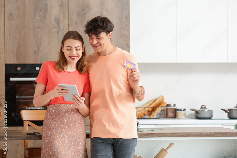 Young couple with tablet computer and gift card shopping online in kitchen