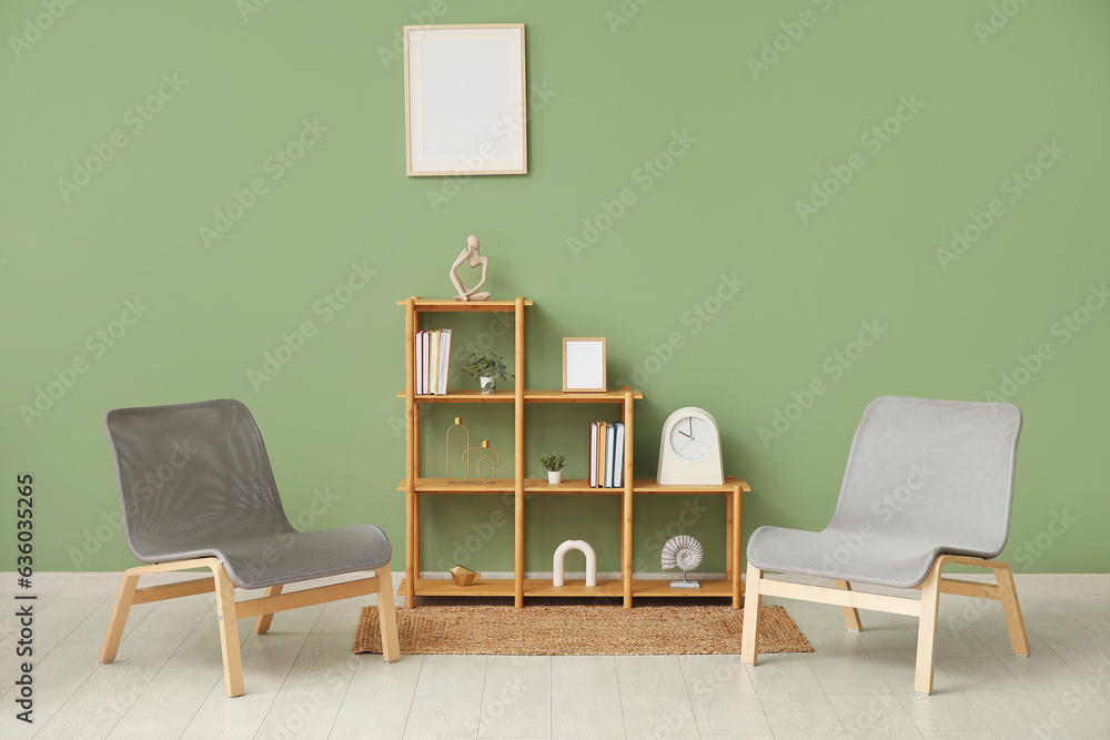 Shelving unit with books, decor, chairs and blank frame hanging on green wall in room