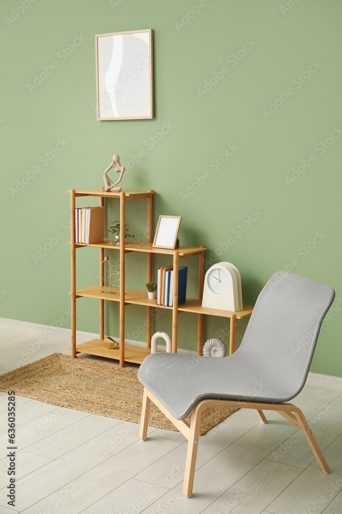 Shelving unit with books, decor, chair and blank frame hanging on green wall in room