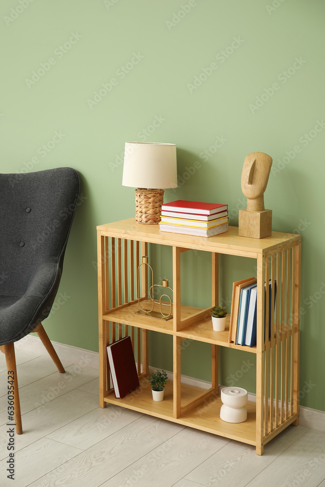 Shelving unit with books, decor and armchair near green wall in room