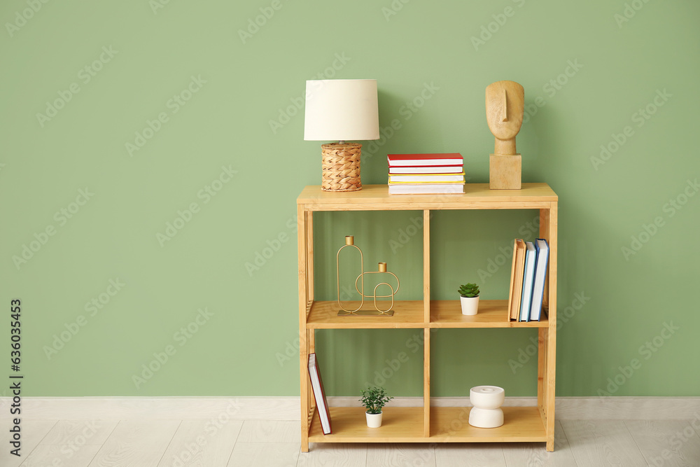 Shelving unit with lamp, books and decor near green wall in room