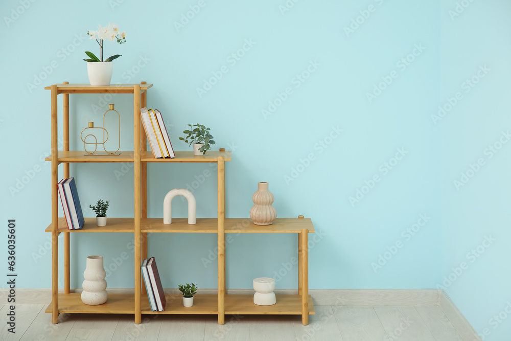 Shelving unit with books, orchid flower and decor near blue wall in room