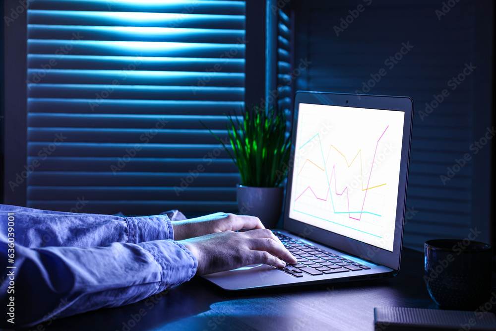 Female programmer typing on laptop keyboard at night in office, closeup