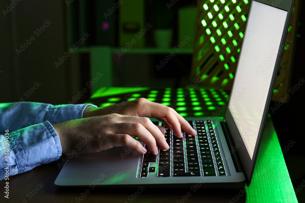 Female programmer typing on laptop keyboard at night in office, closeup