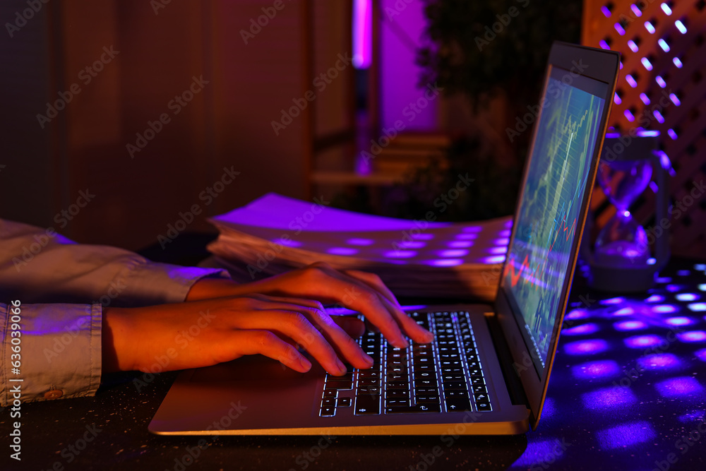 Female programmer typing on laptop keyboard at night in office, closeup