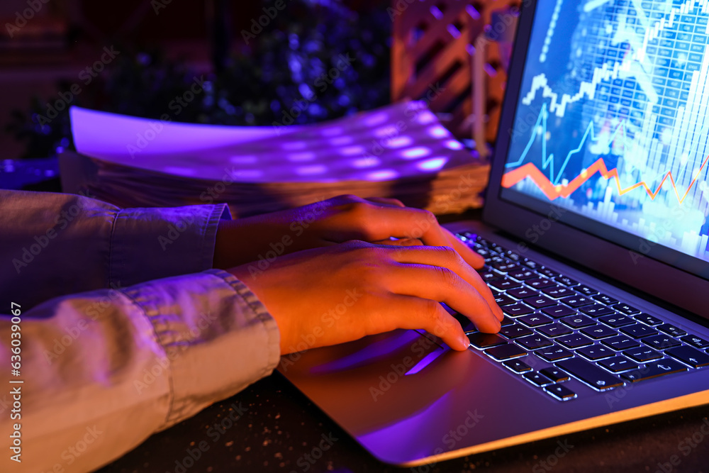 Female programmer typing on laptop keyboard at night in office, closeup