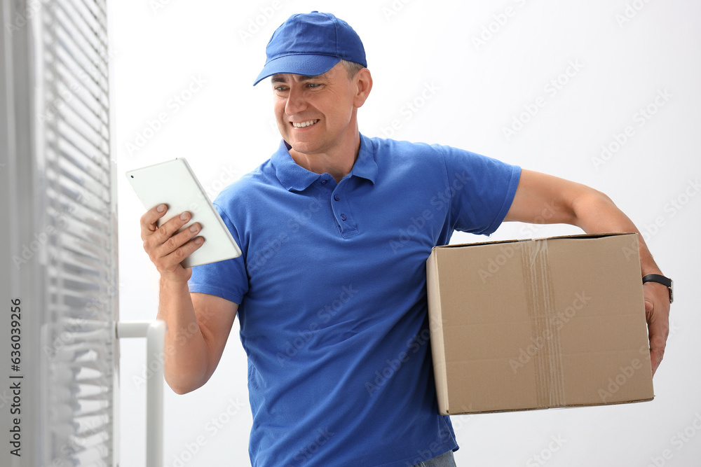 Mature courier with tablet computer and parcel in stairway