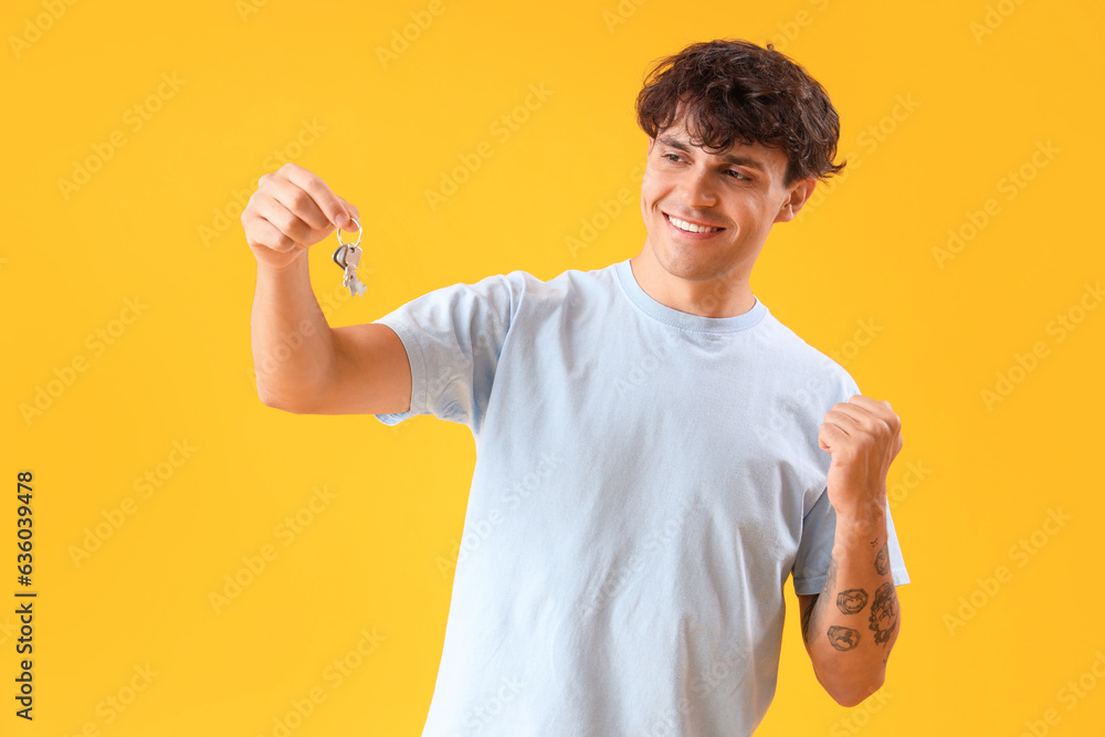 Happy young man with keys from house on yellow background