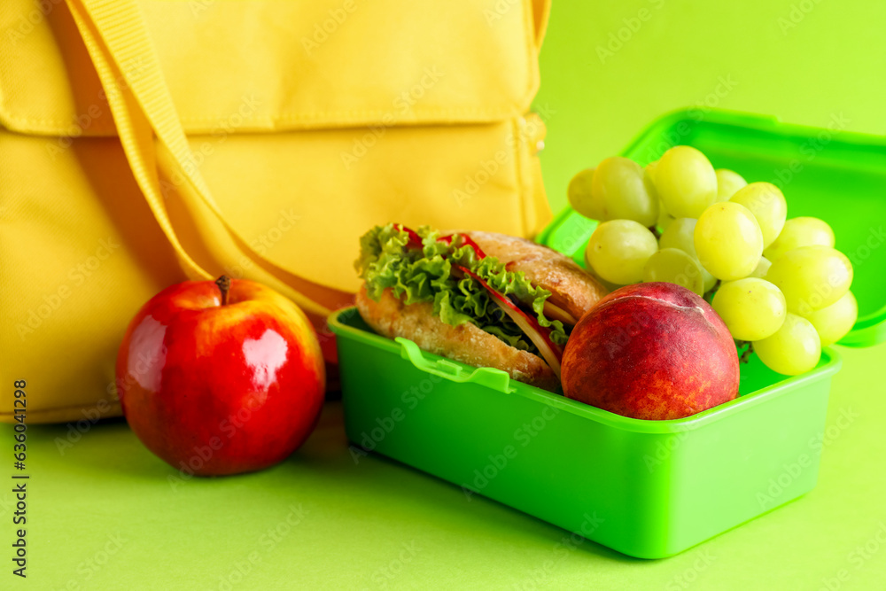 Bag and lunchbox with tasty food on green background