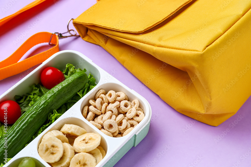 Bag and lunchbox with tasty food on lilac background