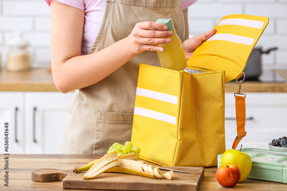 Woman packing bottle of juice into lunch box bag in kitchen