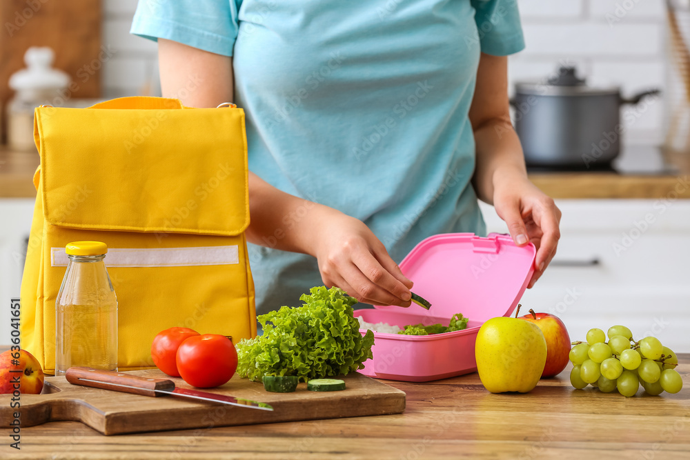 Woman packing fresh meal into lunch box in kitchen