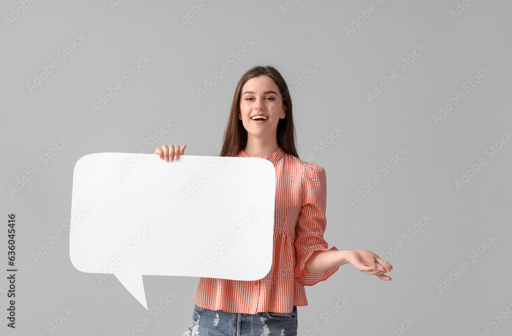 Beautiful happy young woman with speech bubble pointing at something on grey background