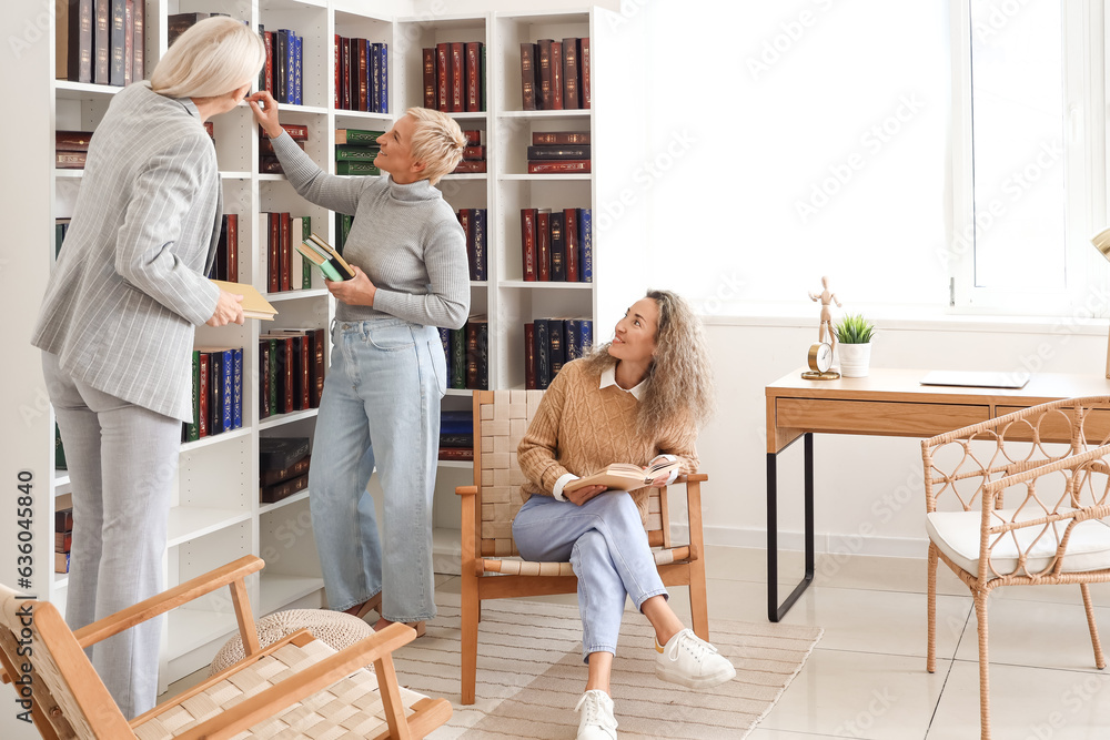 Mature women taking books from shelves at home library