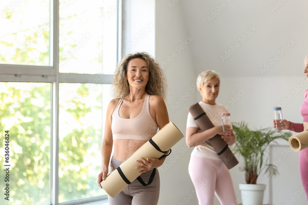 Sporty mature woman with yoga mat in gym