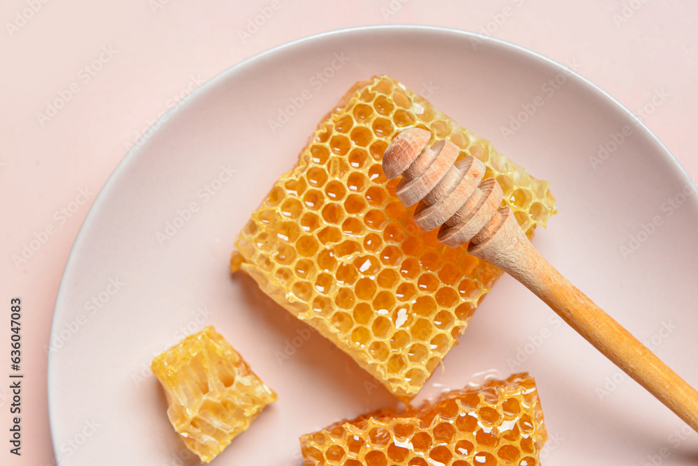 Plate with sweet honeycombs and dipper on pink background