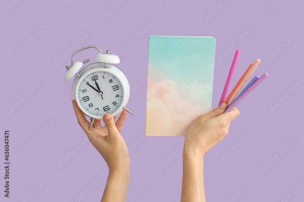 Female hands holding school supplies and alarm clock on lilac background