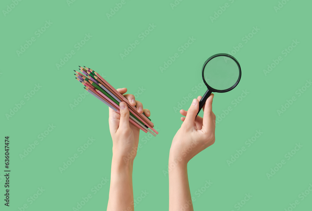 Female hands holding colorful pencils and magnifying glass on green background