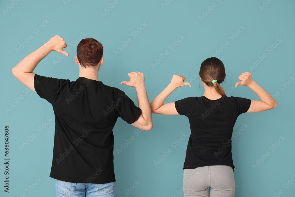 Young couple pointing at their black t-shirts on blue background, back view