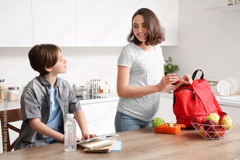 Mother packing lunch in backpack and helping her little son with homework at kitchen