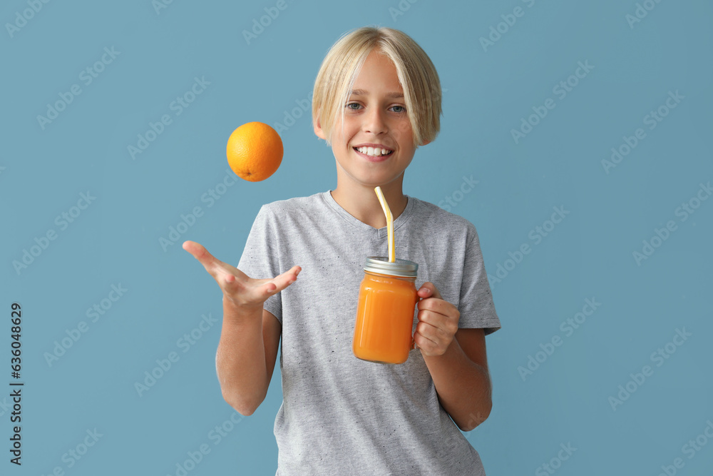 Little boy with glass jar of juice and orange on blue background