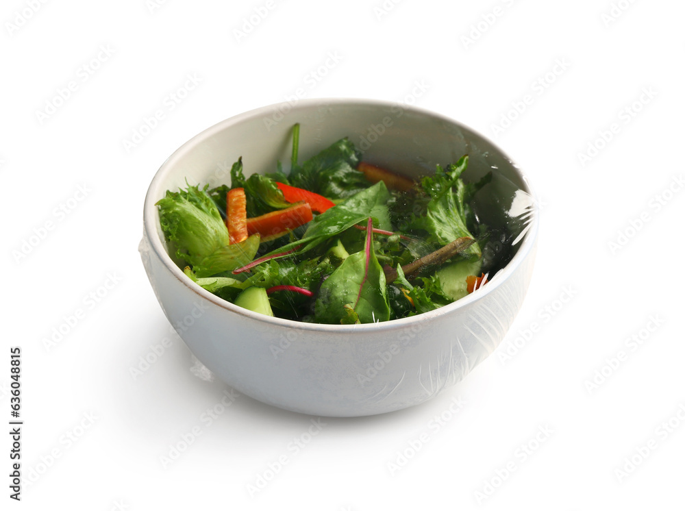 Bowl of fresh salad covered with plastic food wrap on white background